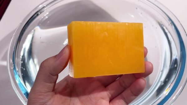 Hand holding a papaya soap bar with natural orange color and smooth texture