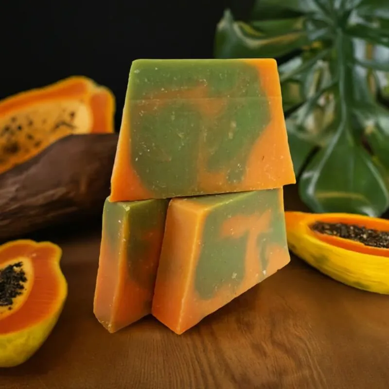 Colorful bars made with homemade papaya soap ingredients displayed beside fresh papaya slices