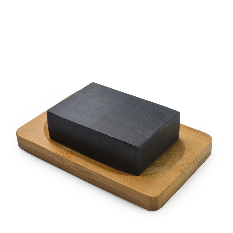 Charcoal soap bar placed on a wooden tray, highlighting its dense black texture and natural formulation